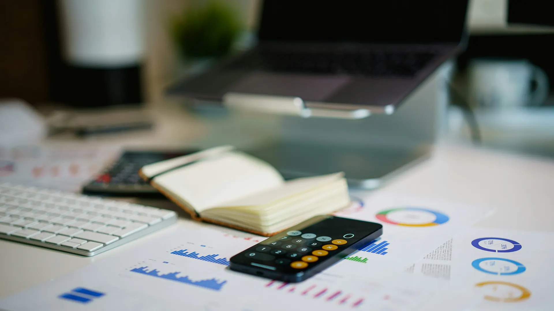 A phone calculator, a notebook and printed charts on a desk