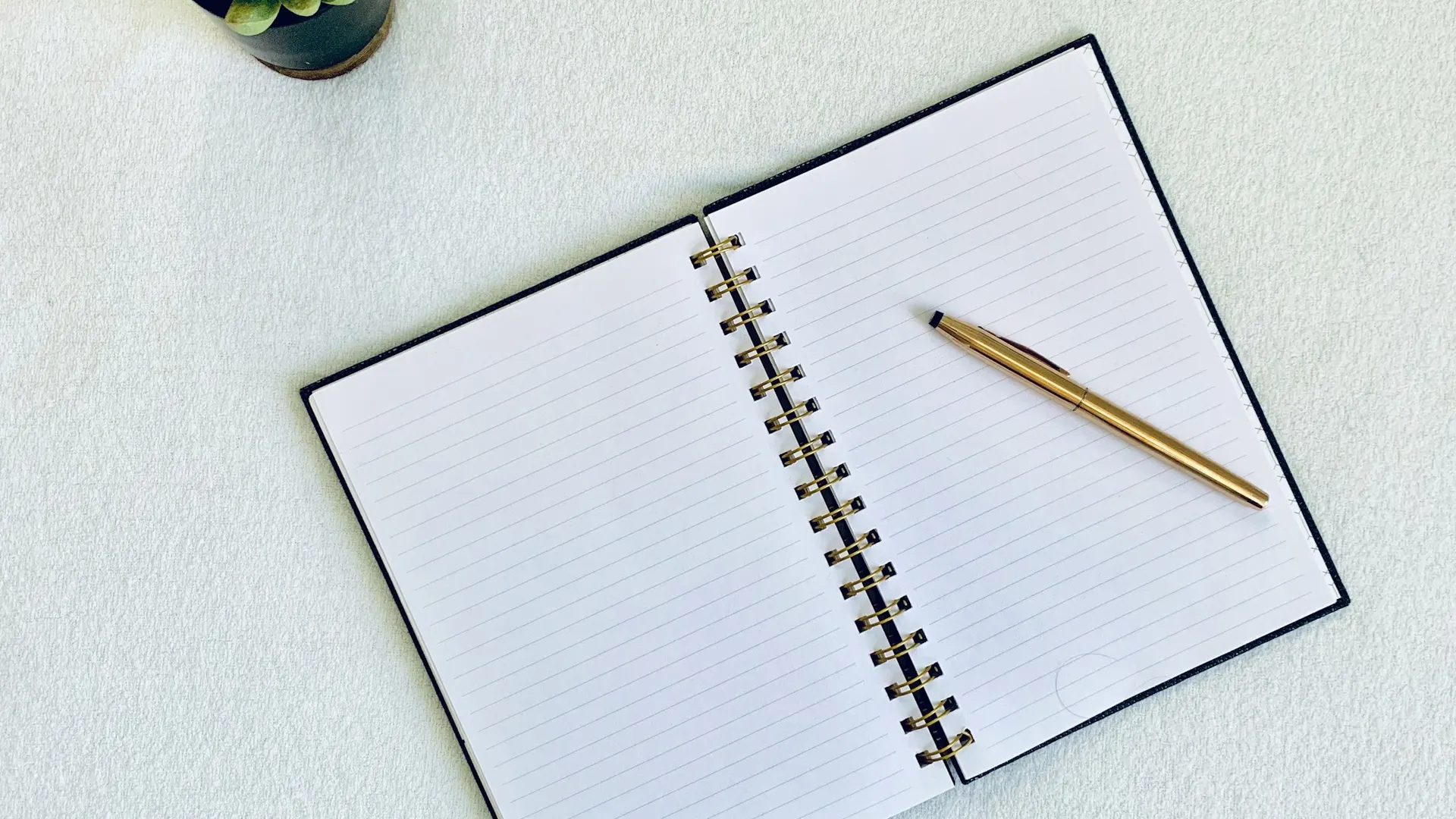An open lined notebook with a gold pen resting on it